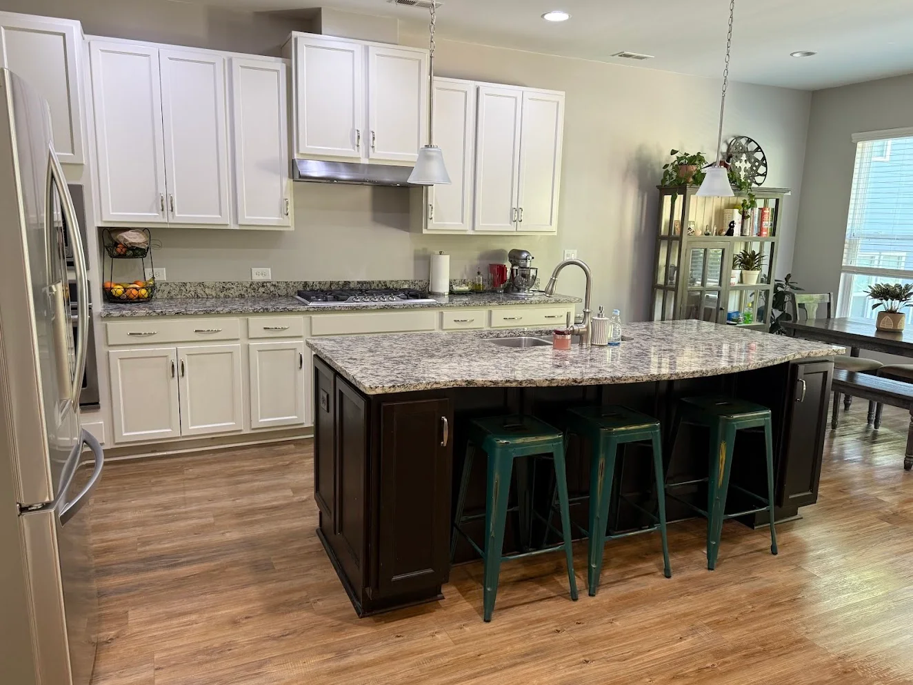 A clean kitchen with white cabinets, granite counters and a dark island with green stools