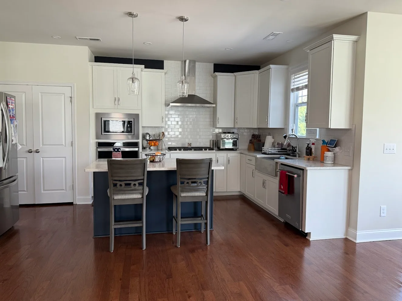An open kitchen with white cabinets, stainless appliances and a navy island with bar stools